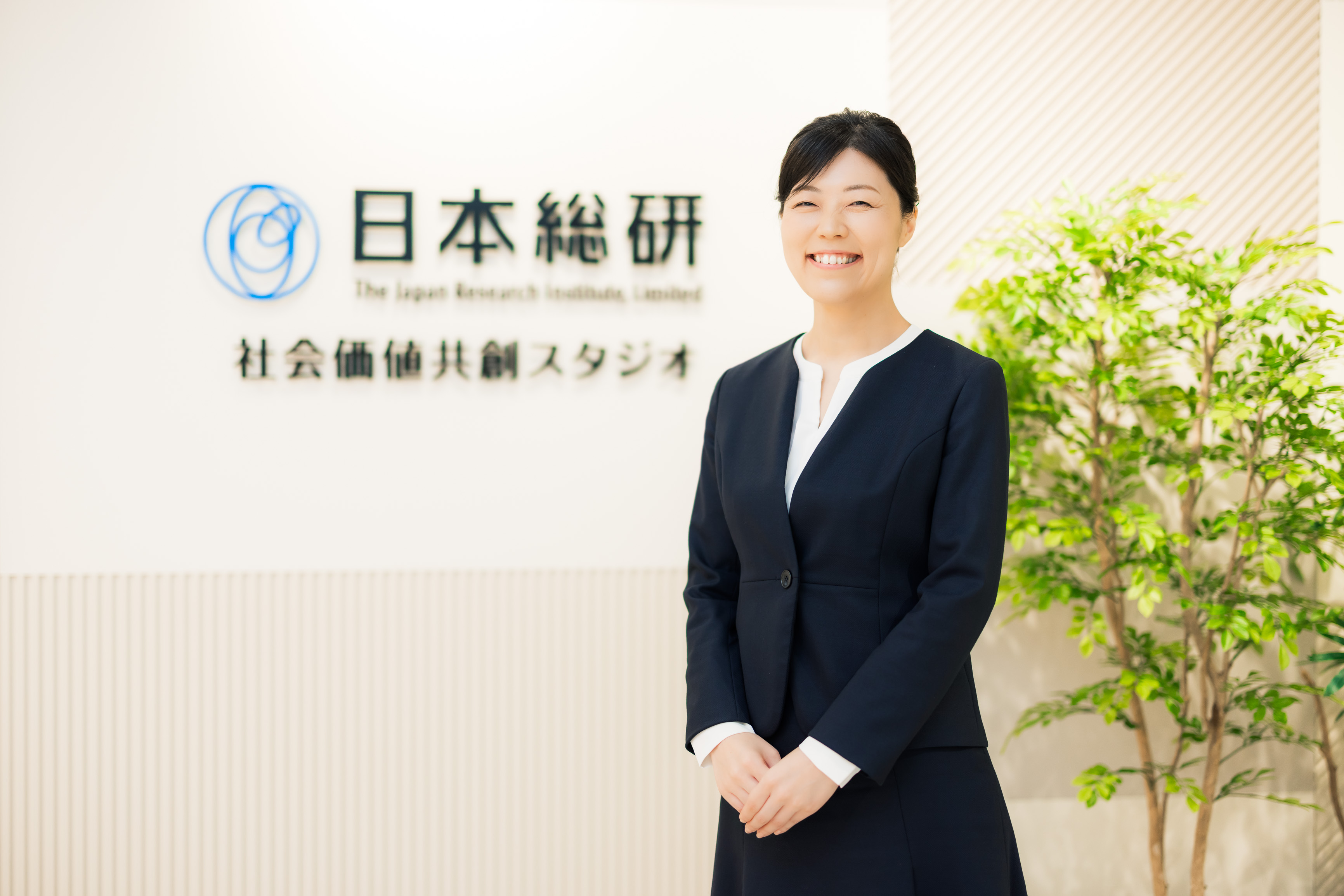 「日本総合研究所 社会価値共創スタジオ」のロゴ前に立つ木下さん