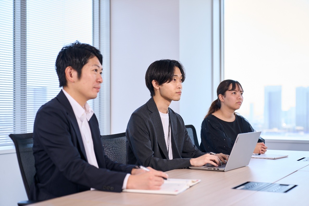 会議室でノートパソコンやノートを使って話を聞く3人の社員